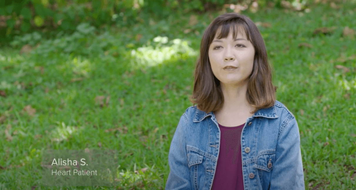 Heart patient Alisha S. talking while sitting in the grass on a hill