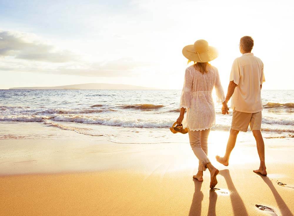 Couple walks on beach at sunrise.
