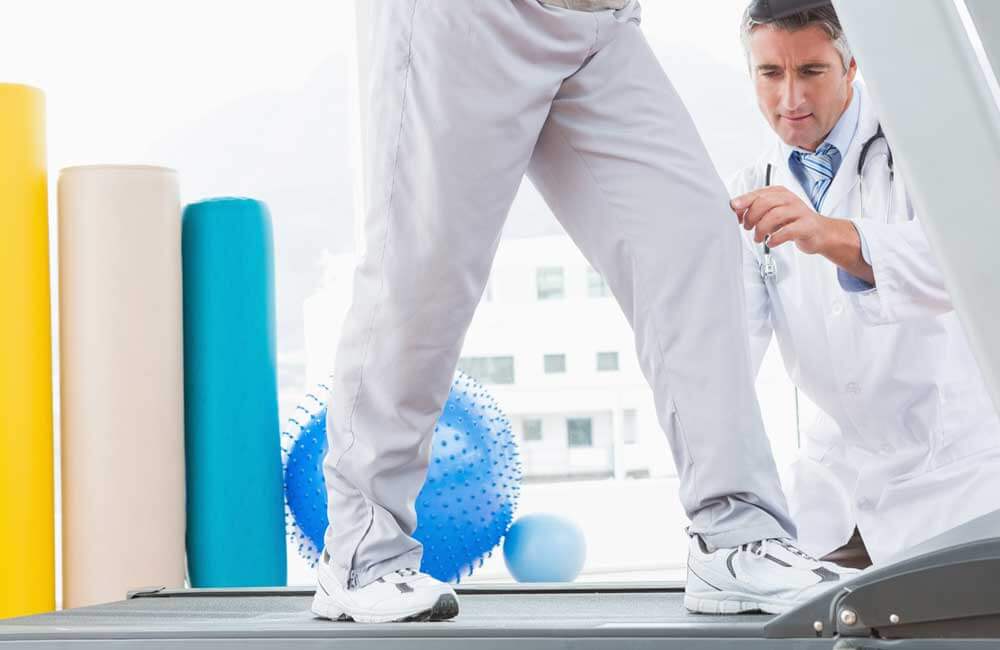 Dcotor exams patients leg as he walks on a treadmill.