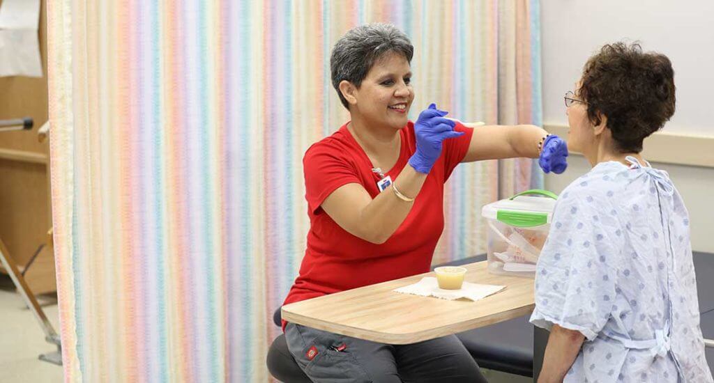 Physical therapist holding feeding apples sauce to a patient