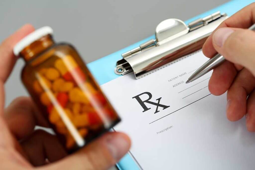 Close up of prescription form with hand holding pen and bottle of pills.