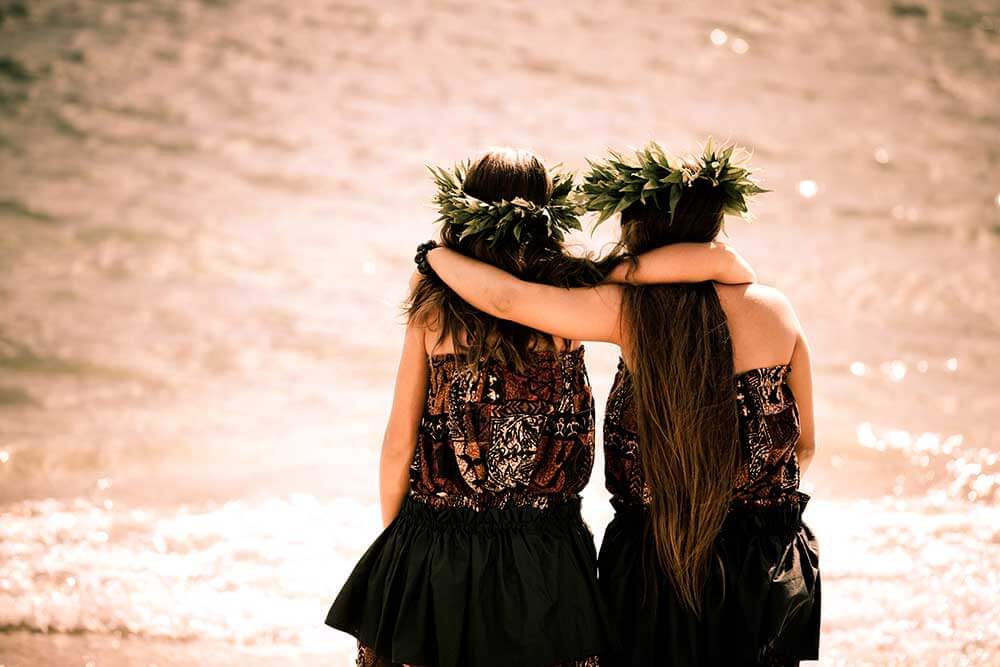 Two girls inhula dresses walking down the beach with arms around each other