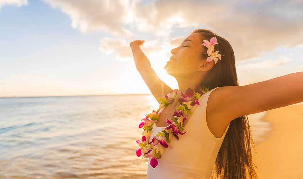 Women spreads out arms and smiles while on the beach at sunset
