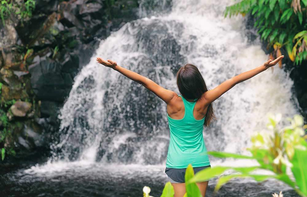 Woman standing with arms open at waterfall.