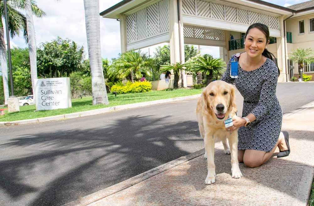 Woman stands with a golden retriever therapy dog in front of the Sullivan Care Center