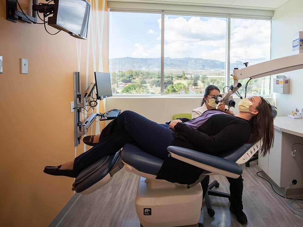Pateint sitting in exam chair with a physician examining her ear.