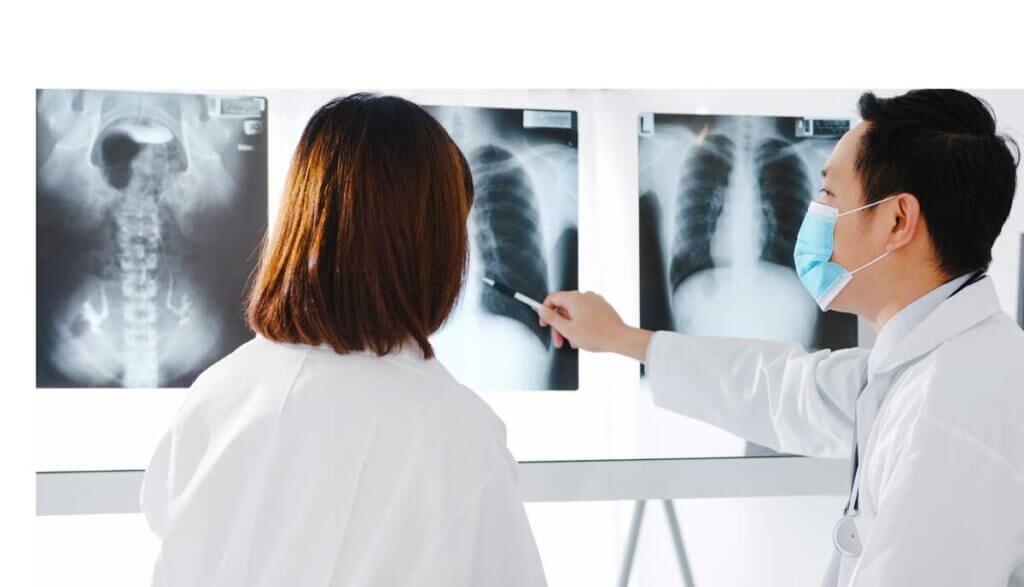 2 physicians study chest X-rays with one pointing to print.