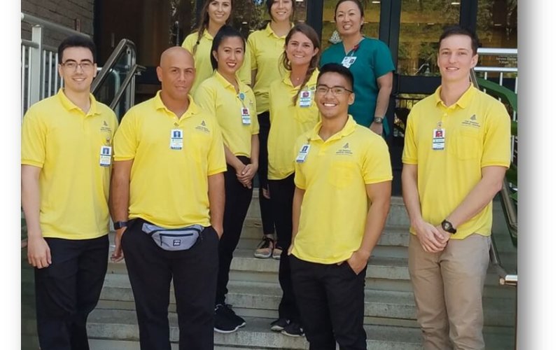 Group of volunteers in yellow shirts standing on the steps of the Queens Medical Center