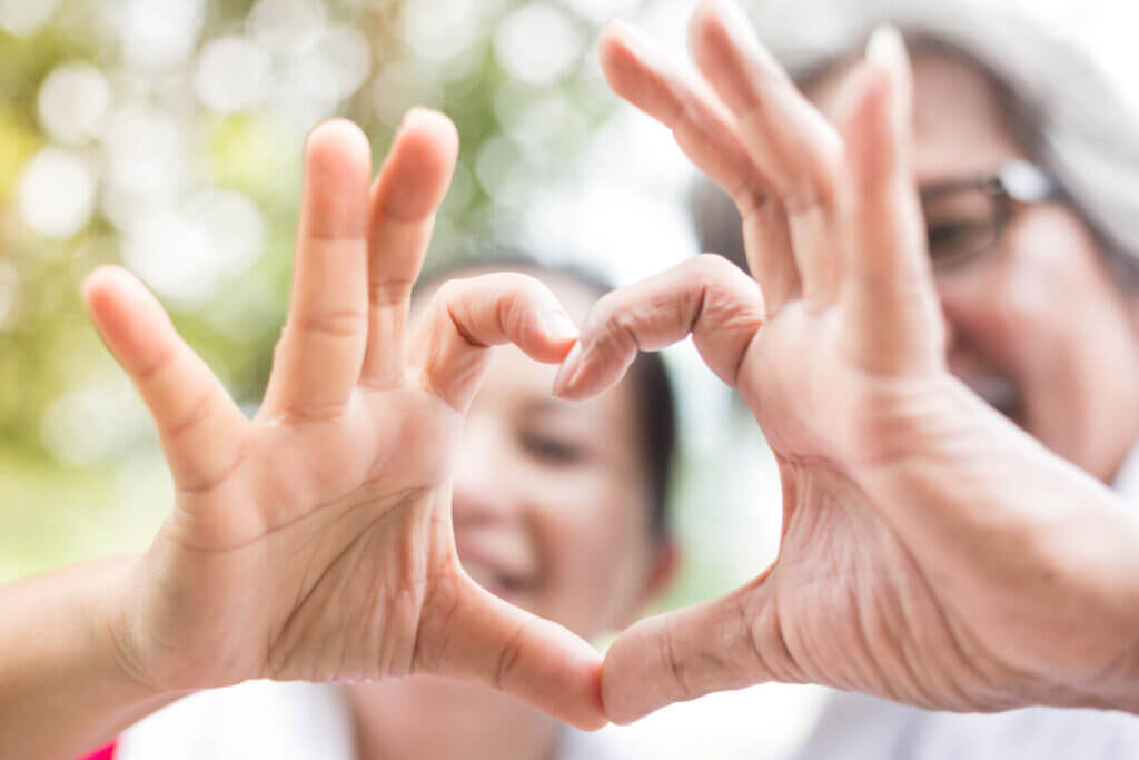Grandparent and child forming a heart with hands